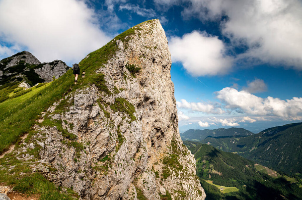 Young woman summer hiker with backpack climbing steep slopes, panoramic peaks and mountains with valleys around. Female trekker in challenging terrain in Karavanke mountains, Slovenia and Karawanken mountains, Carinthia, Austria - Photo, Image