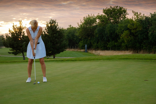 Dama centrada en golpear la bola en el agujero del golf . - Foto, Imagen