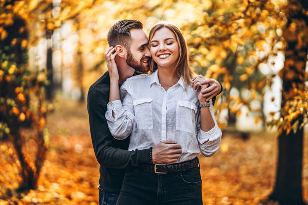 A young couple in love walking in the autumn park on a sunny day. The man gently hugs the woman. Love story. - Valokuva, kuva