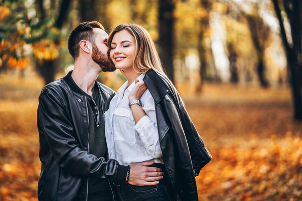 Egy fiatal szerelmespár portréja. Férfi és nő ölelkezik és mosolyog az őszi park hátterében. - Fotó, kép