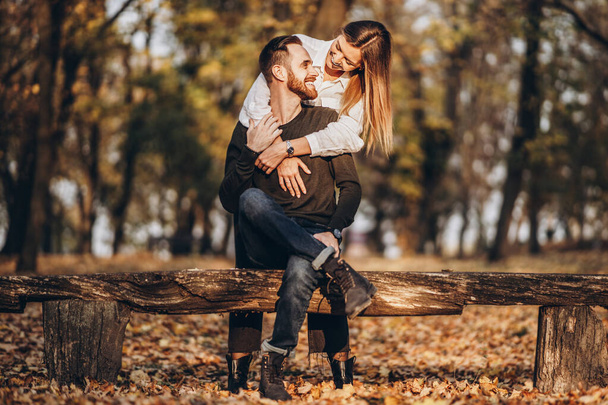 A young loving couple sitting on a wooden bench in the forest. Man and woman hugging and smiling on the background of autumn trees. - Photo, Image