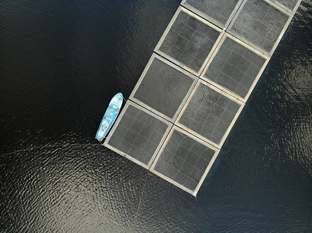 Aérea desde arriba hacia abajo vista de cerca a la granja de peces en el lago. jaulas y barco. - Foto, imagen