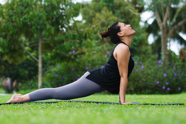 Yoga bhujangasana cobra pose by woman in white costume on green grass in the park - Photo, Image