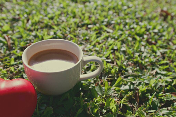 Witte kop hete koffie op het gras met rode hart bal, Stilleven, zachtjes focus - Foto, afbeelding