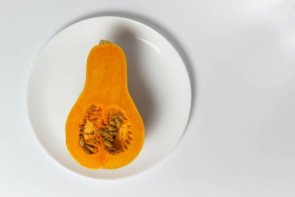 Half pumpkin with seeds on a white plate on a white background. Copy space. Minimalism. Horizontal orientation. - Photo, Image