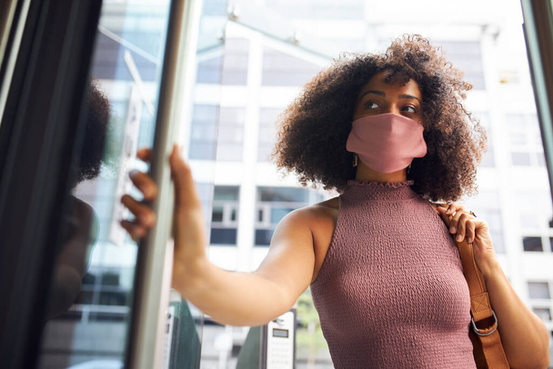 Genç yetişkin bir kadın ofise yüz maskesi takmış kameradan dışarı bakıyor. - Fotoğraf, Görsel
