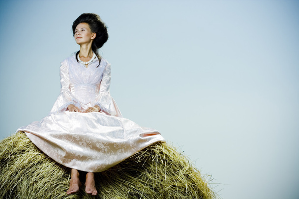 Beautiful woman in vintage dress sitting on haystack - Photo, Image