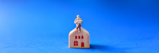 Zakelijk, Hypotheek en Home Lening en informatie Omslagpagina Concept. Close-up van zakenman miniatuur figuur mensen zitten en het lezen van een boek over houten home toy met blauwe achtergrond. - Foto, afbeelding