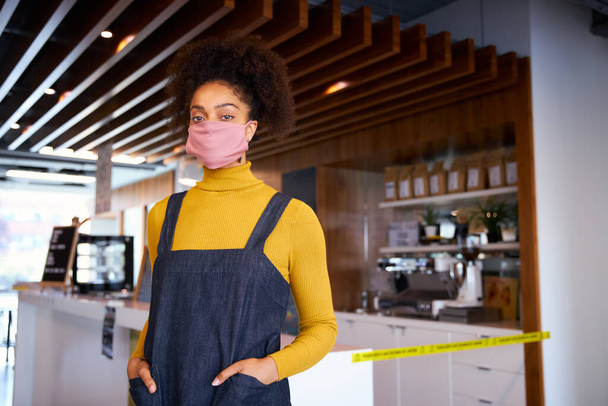 Γυναίκα Αφρικανή ιδιοκτήτρια καφετέριας που φοράει μάσκα προσώπου και στέκεται μπροστά από τον πάγκο - Φωτογραφία, εικόνα