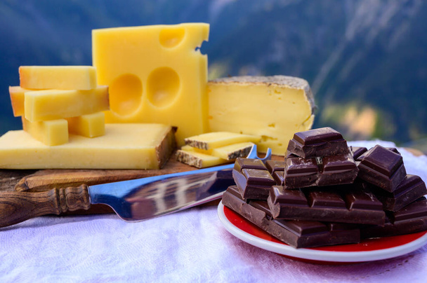 Lekkere Zwitserse kazen en pure pure chocolade, emmentaal, gruyere, appenzeller geserveerd buiten met bergtoppen in de zomer op de achtergrond - Foto, afbeelding