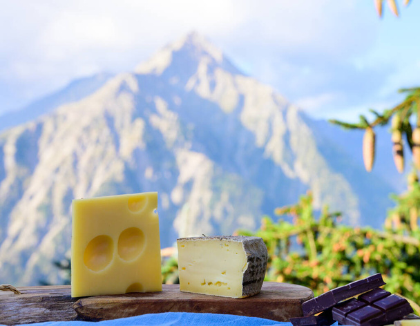 Lezzetli İsviçre peynirleri ve koyu saf çikolata, emmental, gruyere, appenzeller yaz aylarında arka planda Alp dağlarının zirveleriyle birlikte açık havada servis edildi. - Fotoğraf, Görsel