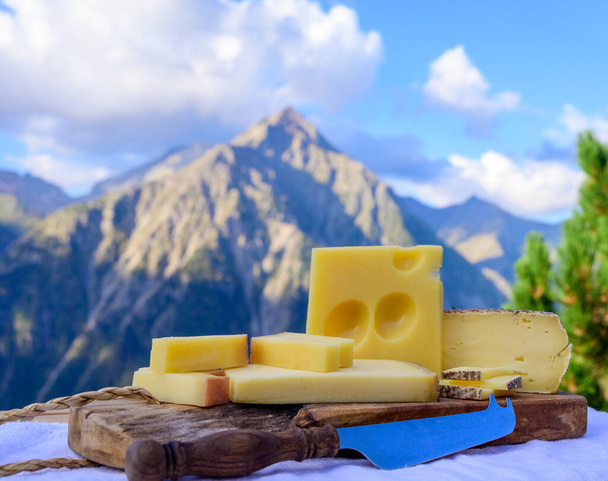 Kaascollectie, Frans beaufort, abondance, emmental, tomme de savoie kazen geserveerd buiten in Savoie regio, met bergtoppen in de zomer op de achtergrond - Foto, afbeelding