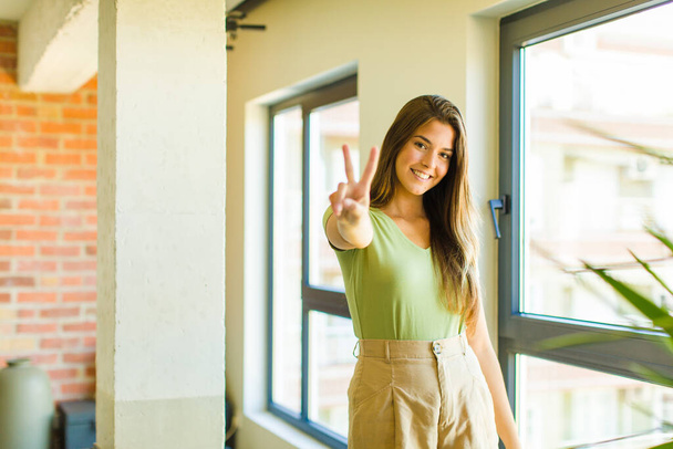 young pretty woman smiling and looking happy, carefree and positive, gesturing victory or peace with one hand - Foto, Bild