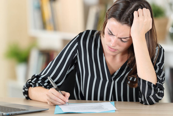 Worried woman signing document sitting on a desk at home - Photo, image