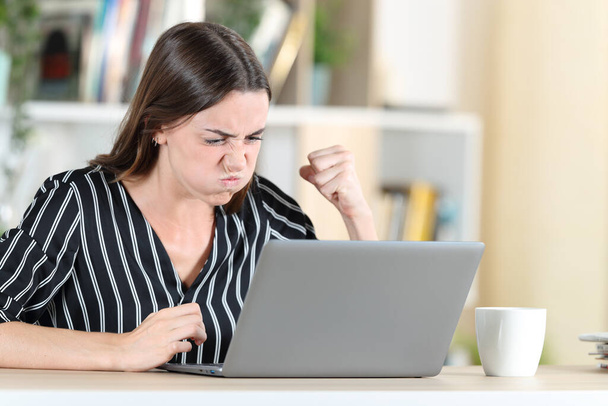 Angry woman checking laptop siting in a desk at home - Фото, изображение
