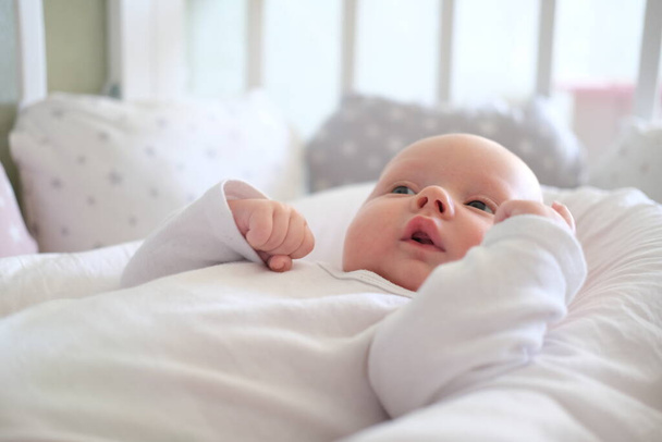 Un bebé recién nacido con ropa blanca yace en la cama. Retrato de un niño mintiendo lindo - Foto, imagen