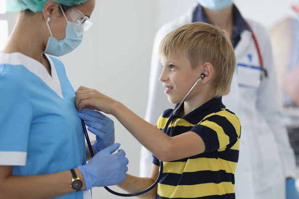 Menino em consultório médico ouve médicos respirar através de estetoscópio - Foto, Imagem