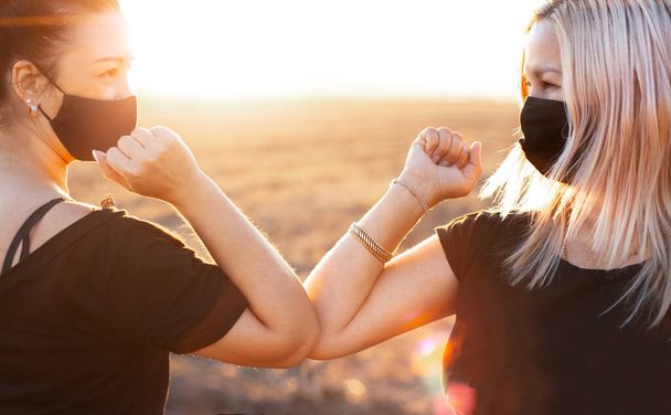 Elbow bump. Two women friends meeting outdoors, on the background of sunset. - Photo, Image