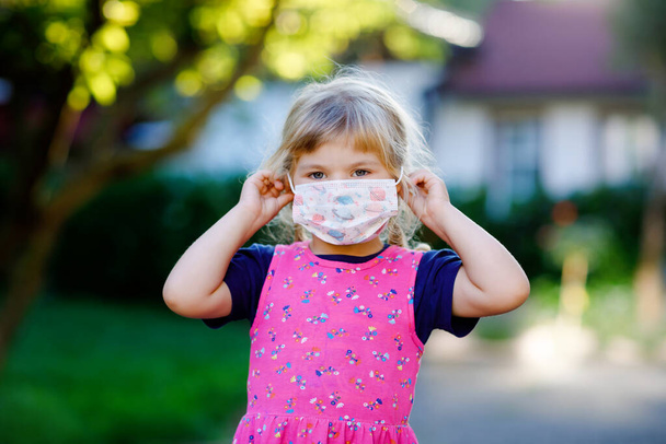 Kleine peuter meisje met medisch masker als bescherming tegen pandemische coronavirus quarantaine ziekte. Schattig kindergebruik en beschermende uitrusting ter bestrijding van covid 19. - Foto, afbeelding