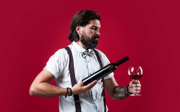 he offers the best. elegant male barman. handsome hipster drinking wine glass. sommelier tasting alcohol. bearded man in suspenders drink red wine. brutal guy bartender in bow tie - Фото, зображення