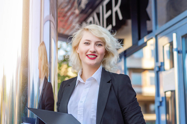 Młoda kobieta biznesu w czarnej kurtce w pobliżu błyszczącej kolumny centrum biznesowego. - Zdjęcie, obraz