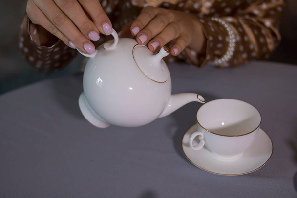 Dziewczyna wlewa herbatę z białego czajnika do białego kubka - Zdjęcie, obraz