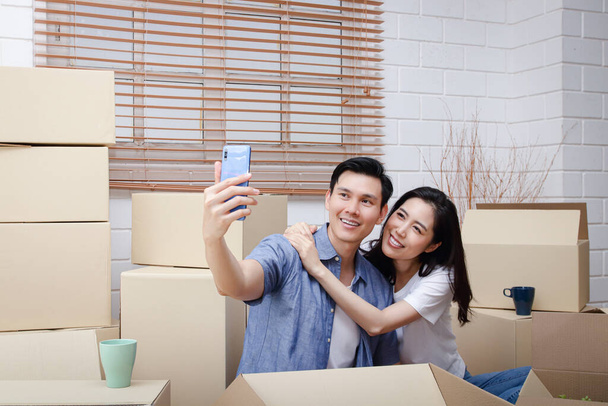 Feliz casal asiático se mudando para uma nova casa Pegue um smartphone e tire uma selfie. Conceito de começar uma nova vida Construir uma família. Espaço de cópia - Foto, Imagem