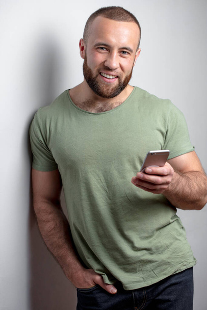 Bearded man in casual clothes looking at phone on white background - Fotoğraf, Görsel