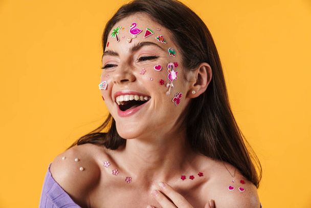 Image of young joyful woman with stickers on face laughing at camera isolated over yellow background - Φωτογραφία, εικόνα