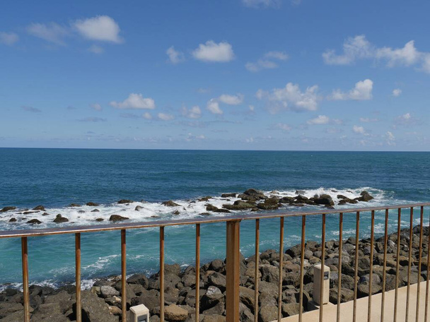 Голубое море с волнами, разбивающимися о скалы, которые видны с перил тротуара в Форт-Эль-Морро в Старом Сан-Хуане, Пуэрто-Рико.  - Фото, изображение