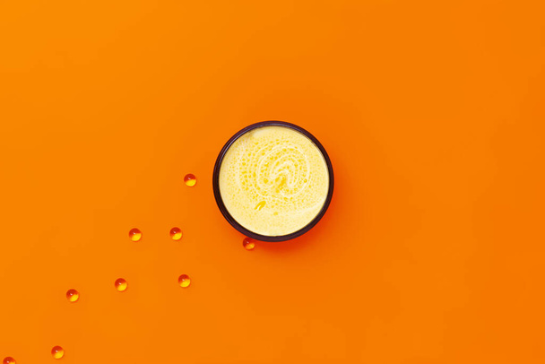 Fekete tégely sárga krém tengeri homoktövis olaj, amely mellett kapszulák E-vitamin narancssárga alapon. - Fotó, kép