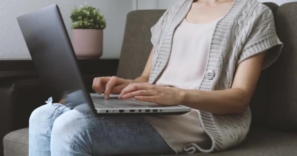 Frau sitzt zu Hause auf Sofa im Wohnzimmer und tippt Laptop-Computer auf Tastatur. Freizeitkleidung - Filmmaterial, Video
