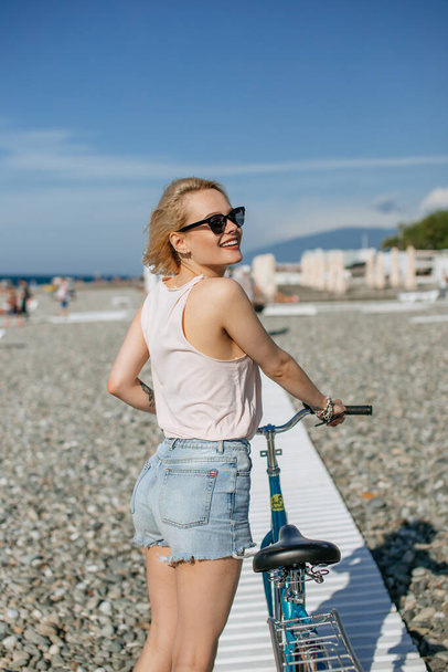 Woman leaning on the bicycle while standing near observation deck on the beach - Foto, imagen