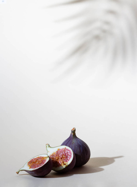 Figs purple fruit, cut on a beige background, shadow from a palm tree, free space - Valokuva, kuva