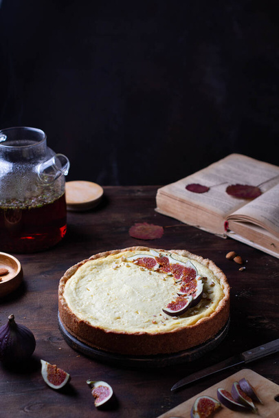 Cheesecake decorated with figs, on a wooden table, next to tea, book, autumn leaves - 写真・画像