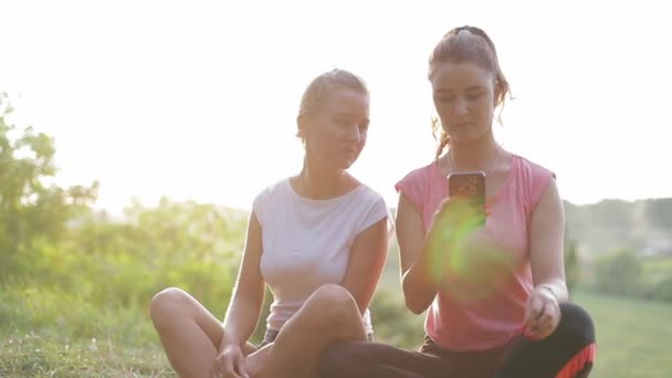 Dos mujeres en un parque de la ciudad utilizan un teléfono inteligente y se comunican entre sí. - Imágenes, Vídeo
