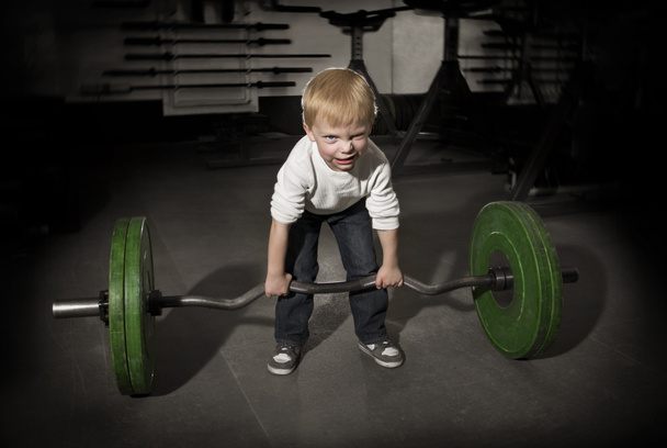 Entschlossener kleiner Junge beim Versuch, schwere Gewichte zu heben - Foto, Bild
