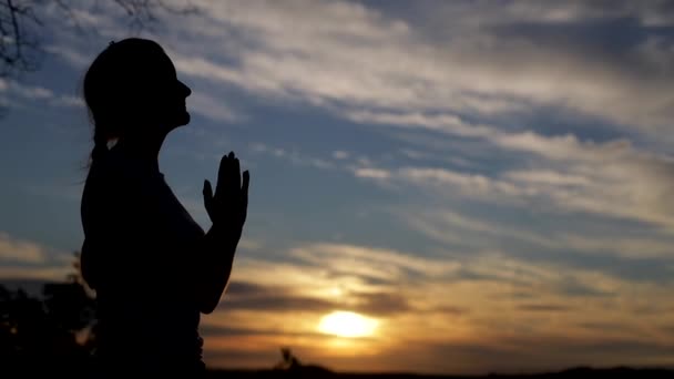 Silhouette di una donna cristiana che prega al tramonto, all'aperto - Filmati, video