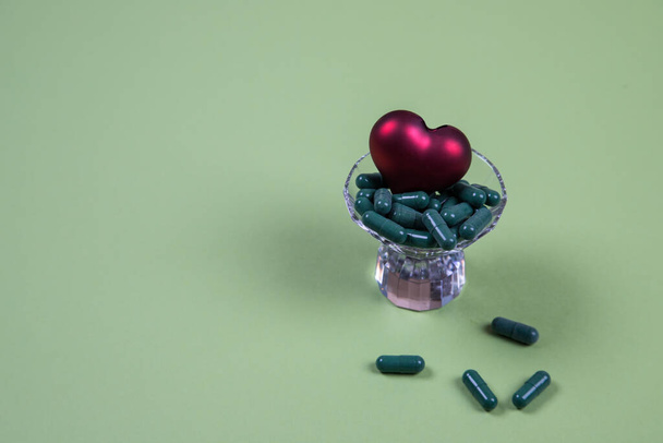Tabletten met een hart in een glazen container op een groene achtergrond, die het leven symboliseren. De werelddag tegen beroerte. Concept. Plaats voor een kopieerruimte - Foto, afbeelding