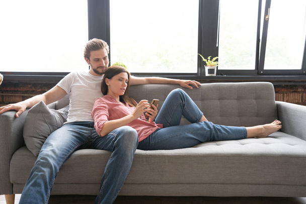 Happy couple enjoying media content in a smart phone sitting on a couch at home. - 写真・画像