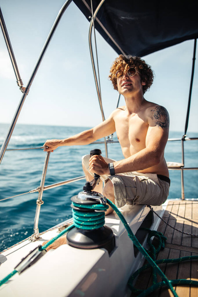 Low angle view of young bearded man standing on the nose yacht - Фото, изображение