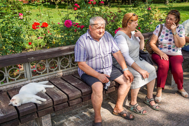 Μια ομάδα ώριμων τουριστών χαλαρώνουν σε ένα πάρκο της πόλης κάθεται σε ένα παγκάκι - Φωτογραφία, εικόνα
