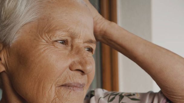 Πορτρέτο μιας ηλικιωμένης μοναχικής γυναίκας που κοιτάζει από το παράθυρο. - Φωτογραφία, εικόνα