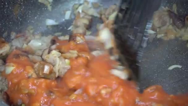 4K video recept voor het maken van saus, dressing of jus met stukjes vlees, uien en tomatenpasta in een koekenpan bij hoge temperatuur close-up.Het proces van het koken van etenswaren, een recept voor het koken van vlees - Video