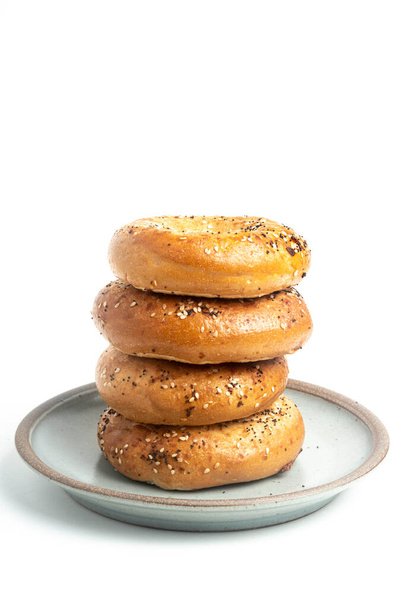 A single tall stack of 4 everything bagels on a ceramic plate set on plain white background.  - Photo, Image