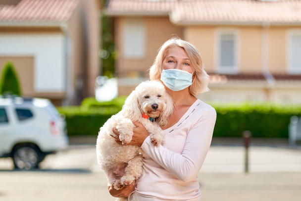 Oudere vrouw met een hond buiten een antivirus masker. - Foto, afbeelding