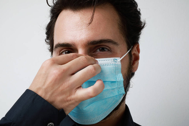 Man wearing protect medical mask. Young man stands on light background and looking aside. Free space for text. - Φωτογραφία, εικόνα