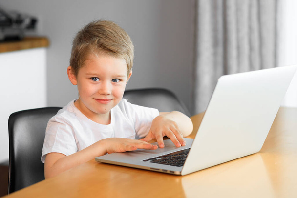 Funny young boy using a laptop computer sitting on top of a table at home - Foto, Bild