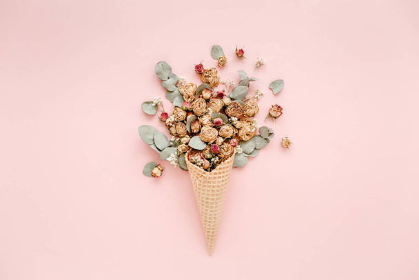 Waffle cone with cotton bouquet and eucalyptus leaves on pink background, flat lay, top view - Foto, afbeelding