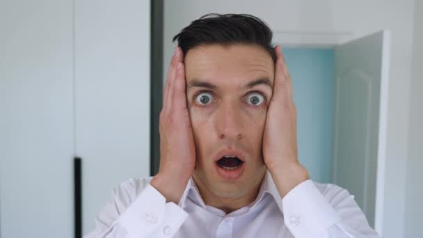 Portrait of scared businessman looks into camera with startle at face clutches his head showing fear and panic. Shocked young man on office background. - Footage, Video